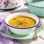 Bol de soupe aux pois à la mijoteuse avec morceaux de carottes et céleri, servie sur une assiette verte