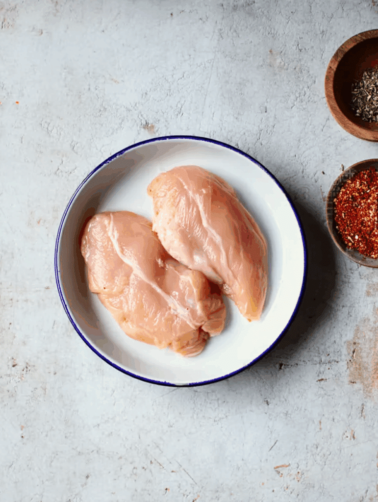 Blancs de poulet crus dans une assiette avec épices en arrière-plan